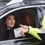 Driver hands a speeding ticket to a police officer through car window.