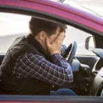 Stressed man sitting in car covering his face while holding the steering wheel.