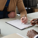 Injured man in an arm sling signs paperwork with a lawyer at an office desk.