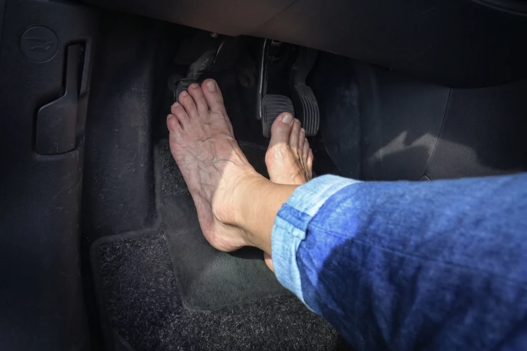 Low-angle view of a driver's bare feet positioning to press the clutch, brake, and accelerator pedals in a car.