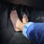 Low-angle view of a driver's bare feet positioning to press the clutch, brake, and accelerator pedals in a car.