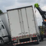 Tow truck recovering a crashed semi-truck on a highway.