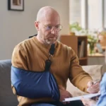An injured man with his arm in a sling, reviewing paperwork with a woman.