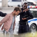 Police officers arresting a handcuffed man near a police vehicle.