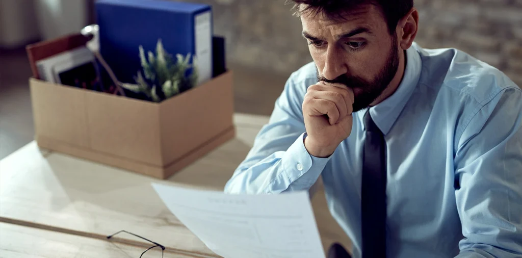 A concerned man looks at a document beside packed boxes.