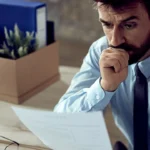 A concerned man looks at a document beside packed boxes.
