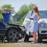 two drivers standing next to damaged vehicles after a car accident.